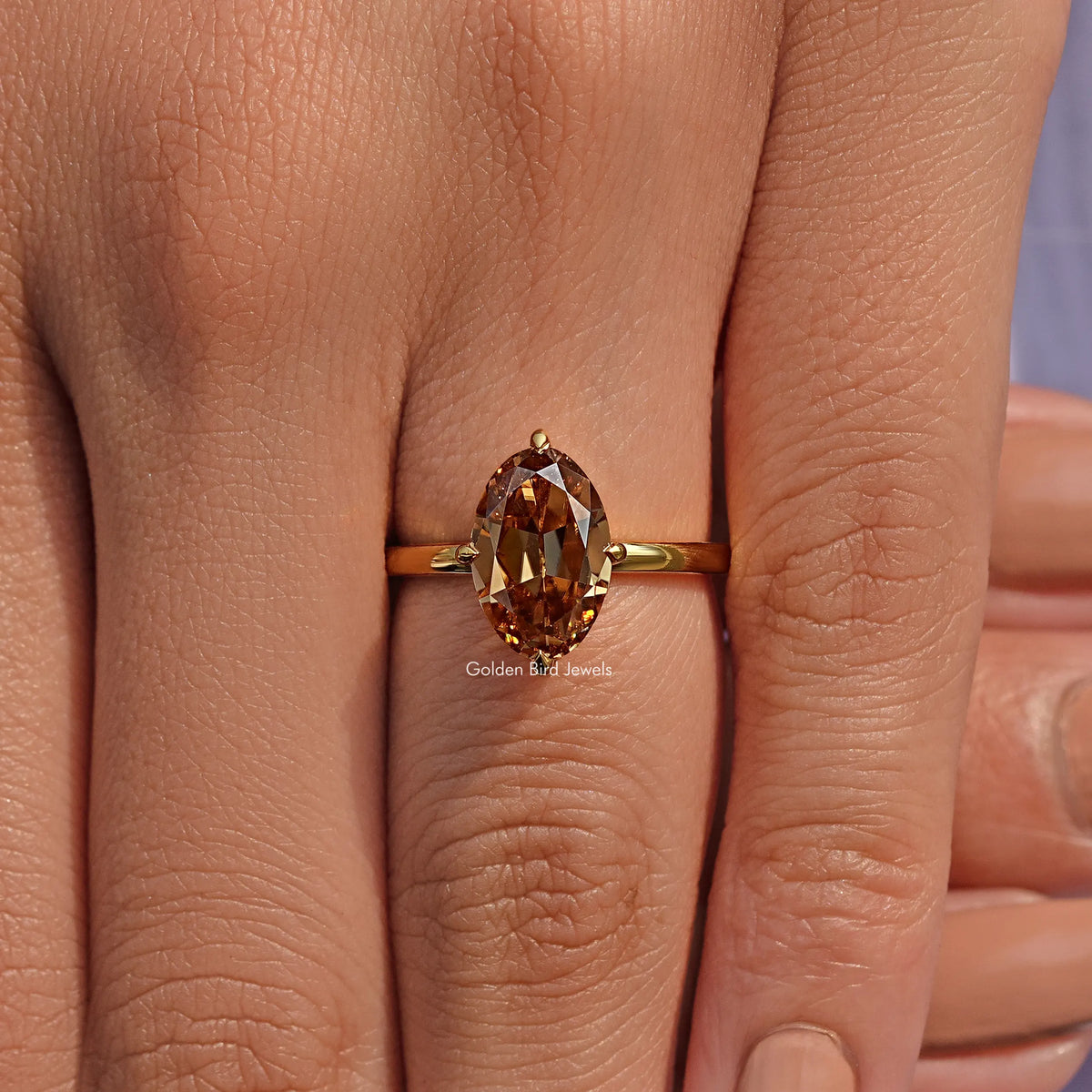 Champagne oval moissanite solitaire ring on hand, gold-tone band and oval center stone