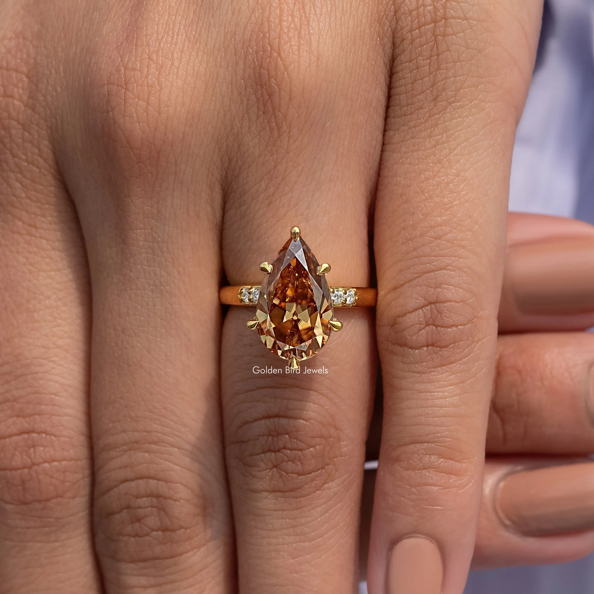 Gold pear-cut engagement ring with warm brown center stone and side prong settings