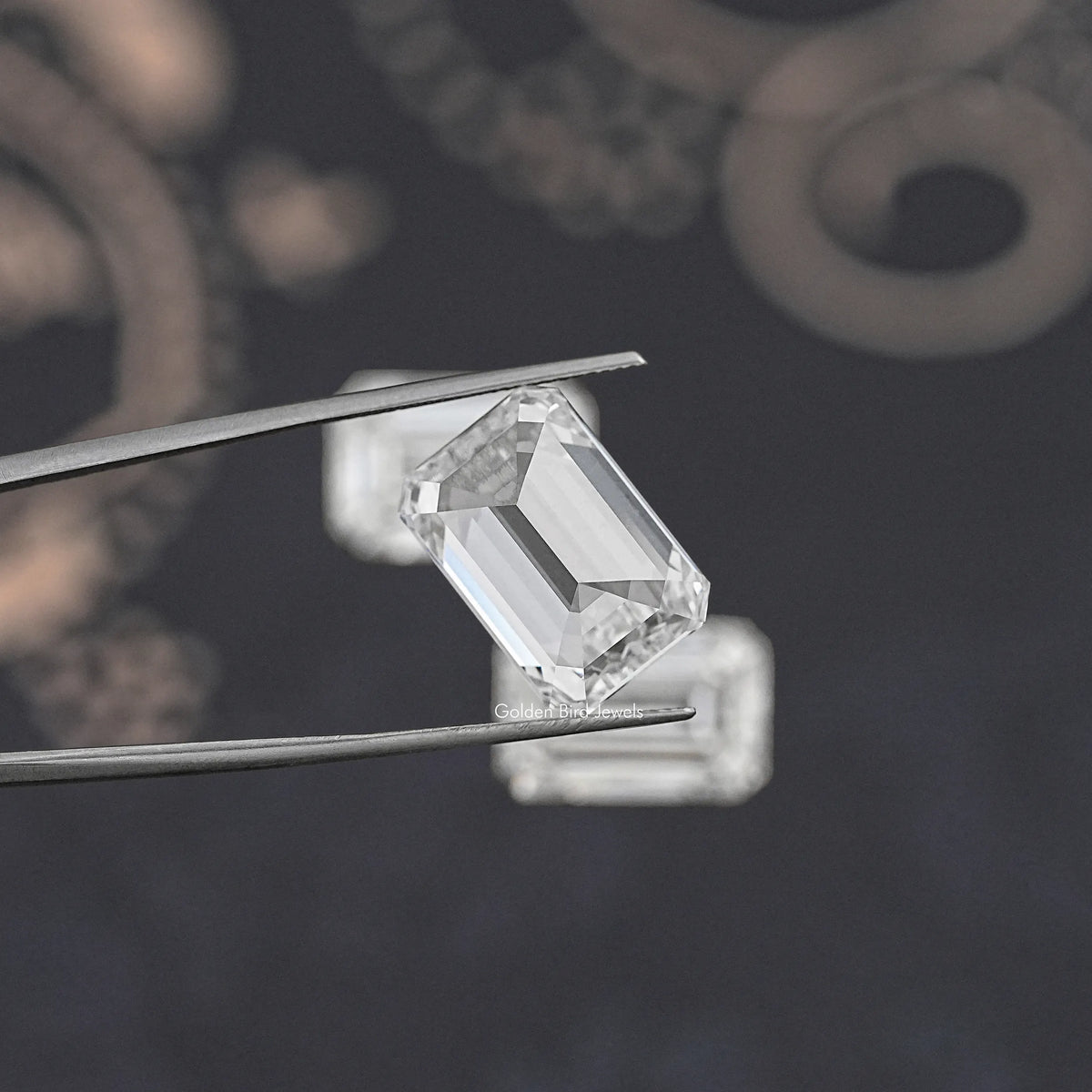 Emerald-cut lab diamond held between metal tweezers, clear faceted step design.