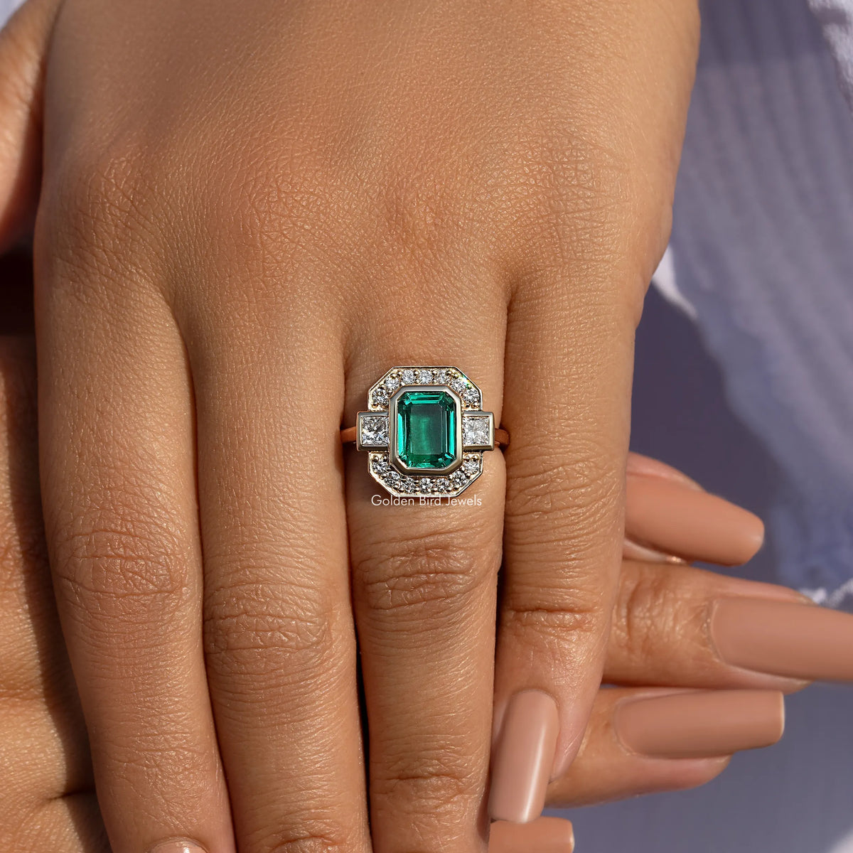 Gold-tone halo ring on hand, emerald-green center stone with clear stone frame