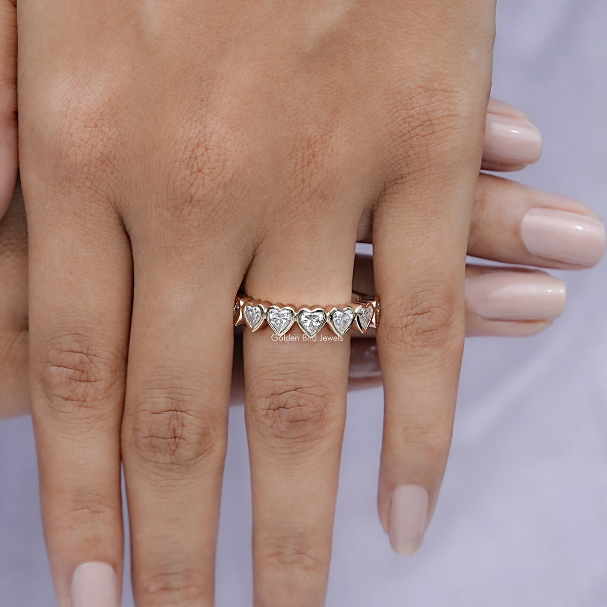 Heart-shaped eternity band ring with bezel-set heart stones, worn by hand