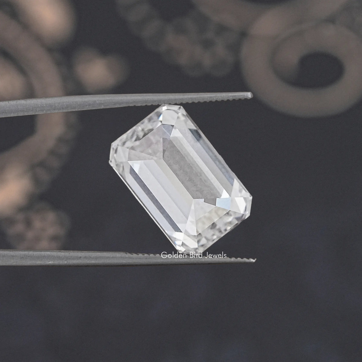 Emerald-cut loose lab diamond, clear, angled on metal tweezers.