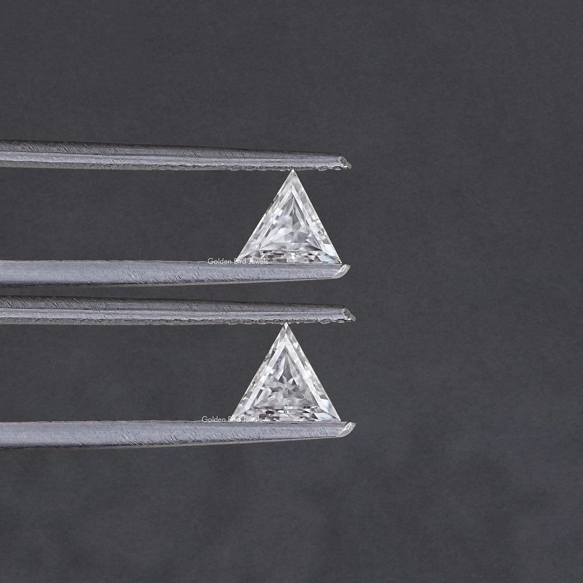 Triangle-cut clear moissanite stones held in silver tweezers, pair