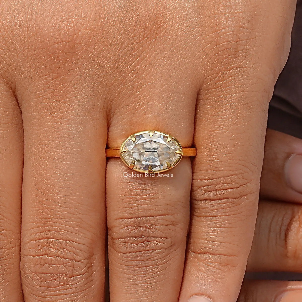 Oval moissanite solitaire ring on fingers, centered oval stone in a gold-tone setting.
