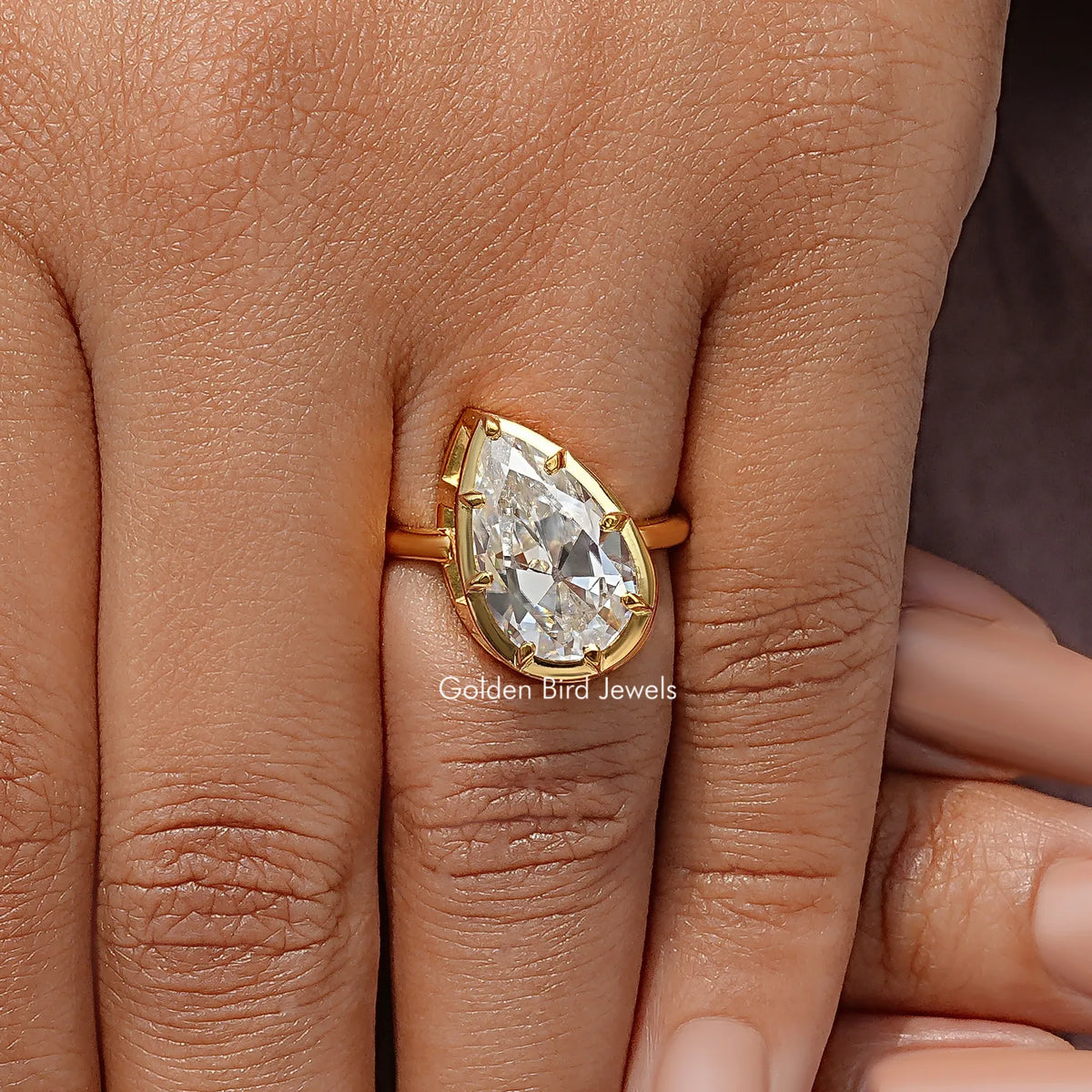 Gold-tone pear-cut solitaire ring on fingers, prong-set center gemstone