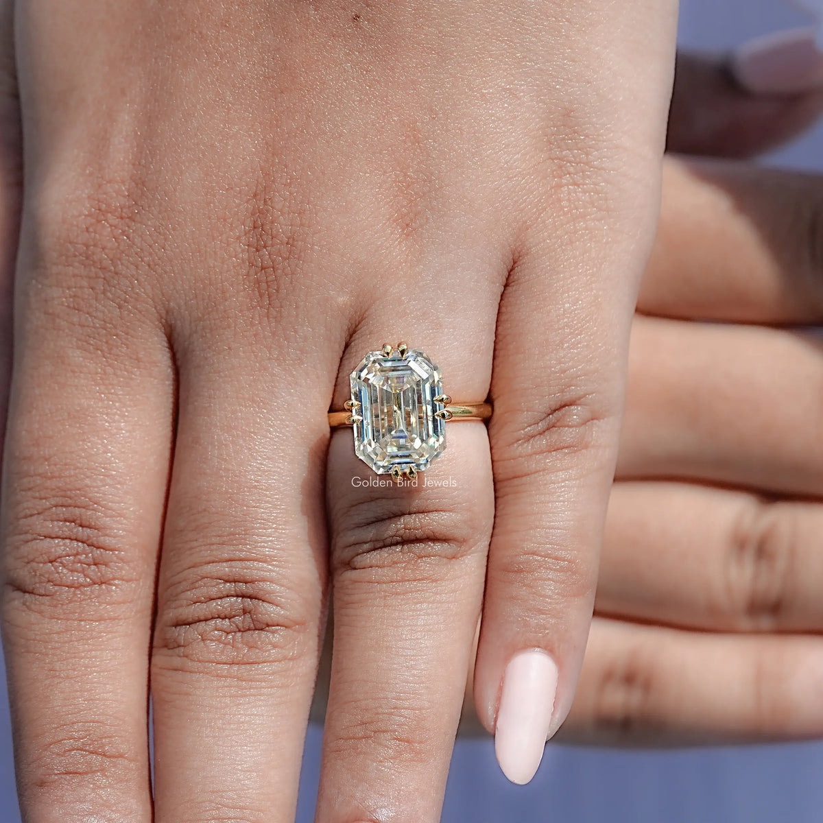 Gold-tone solitaire ring with emerald-cut clear stone on hand