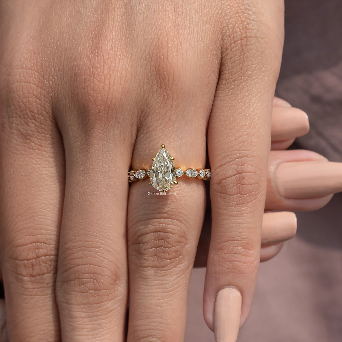 Pear-cut moissanite engagement ring with round side stones on a slim gold-tone band