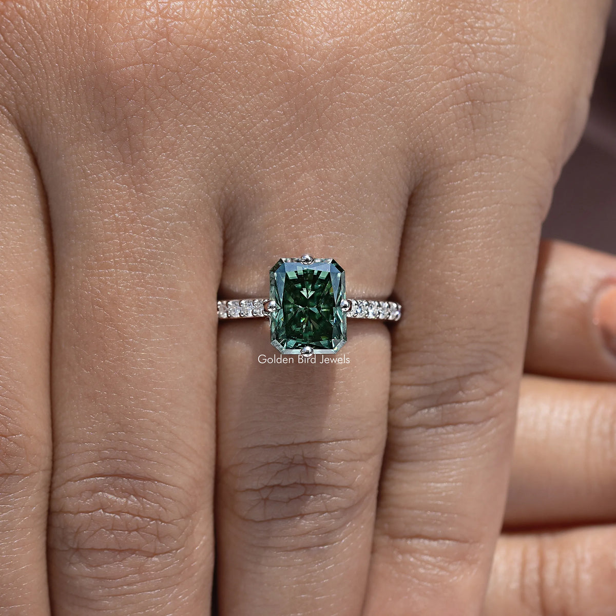 Moissanite solitaire ring showing dark green emerald-cut center and baguette-style side stones