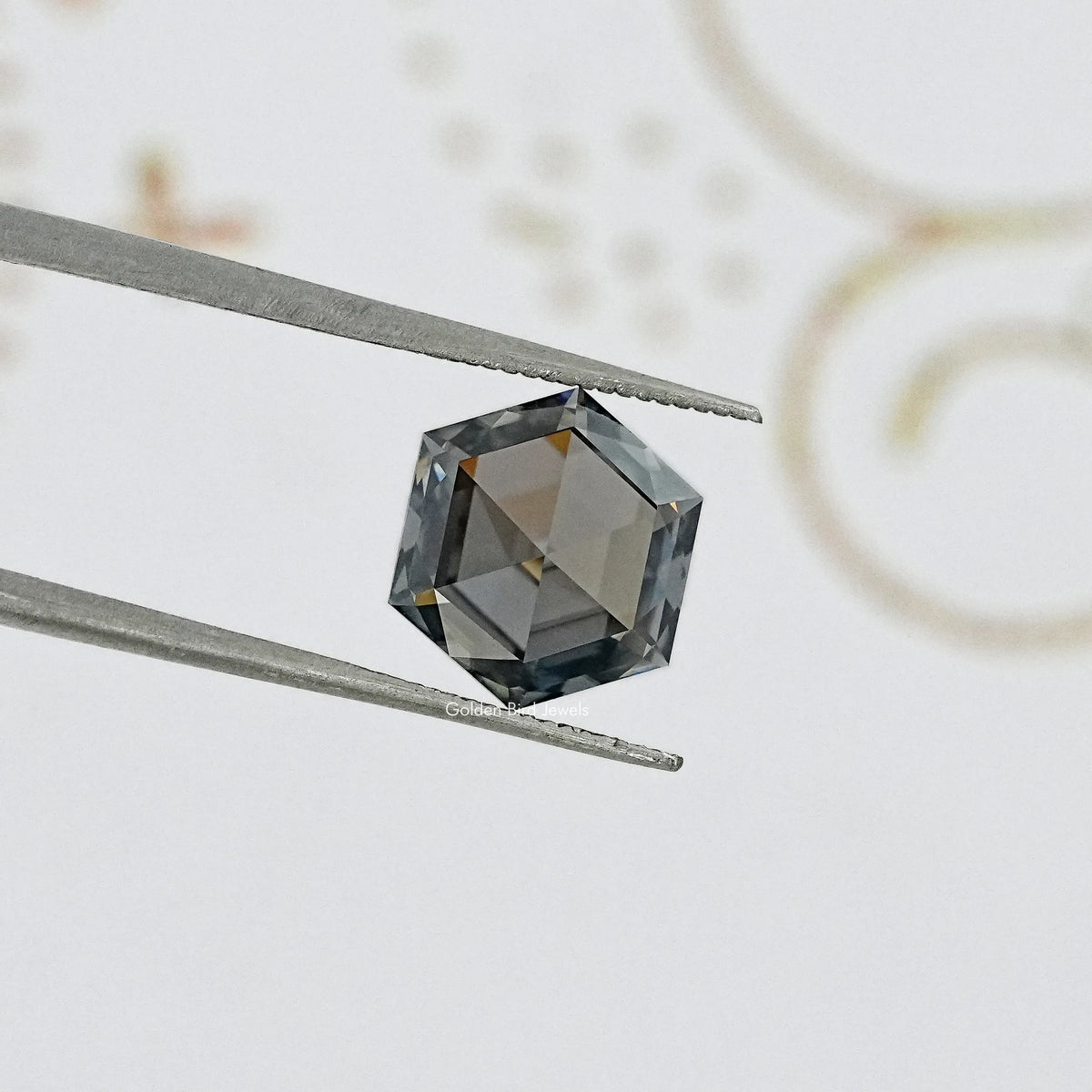 Hexagon-cut gray moissanite gemstone held by tweezers, reflective faceted crown