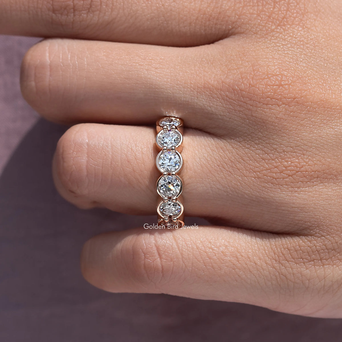 Close-up of bezel-set round diamond wedding band with three stones on finger
