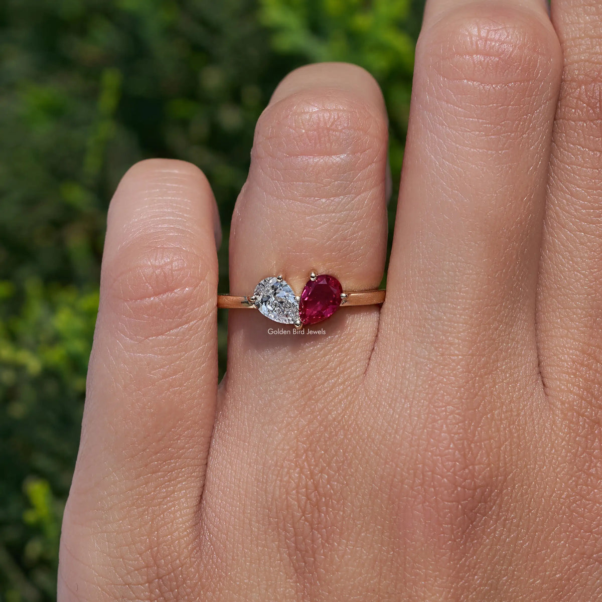 Gold-tone engagement ring on finger with round diamond and red pear-cut center gemstone