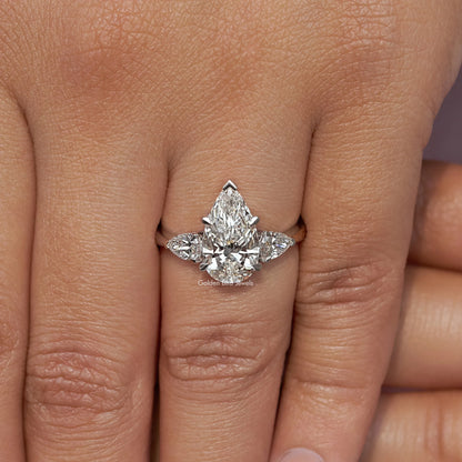 Three-stone pear-cut diamond engagement ring on hand, side stones around center pear
