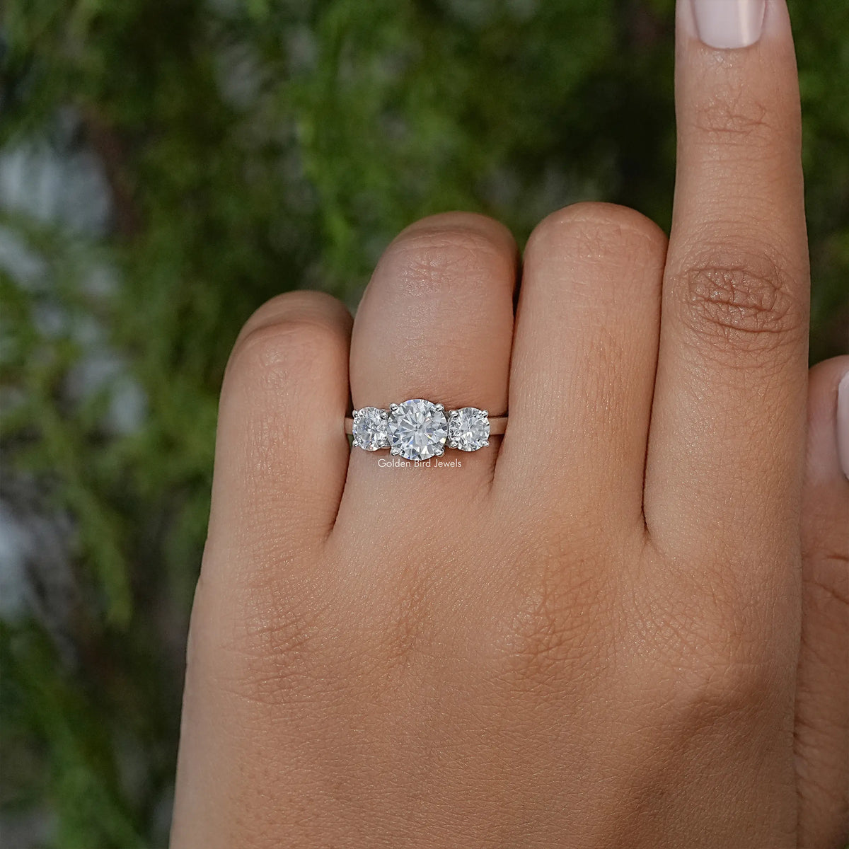 Three-stone moissanite ring on finger with round center stone and two side stones