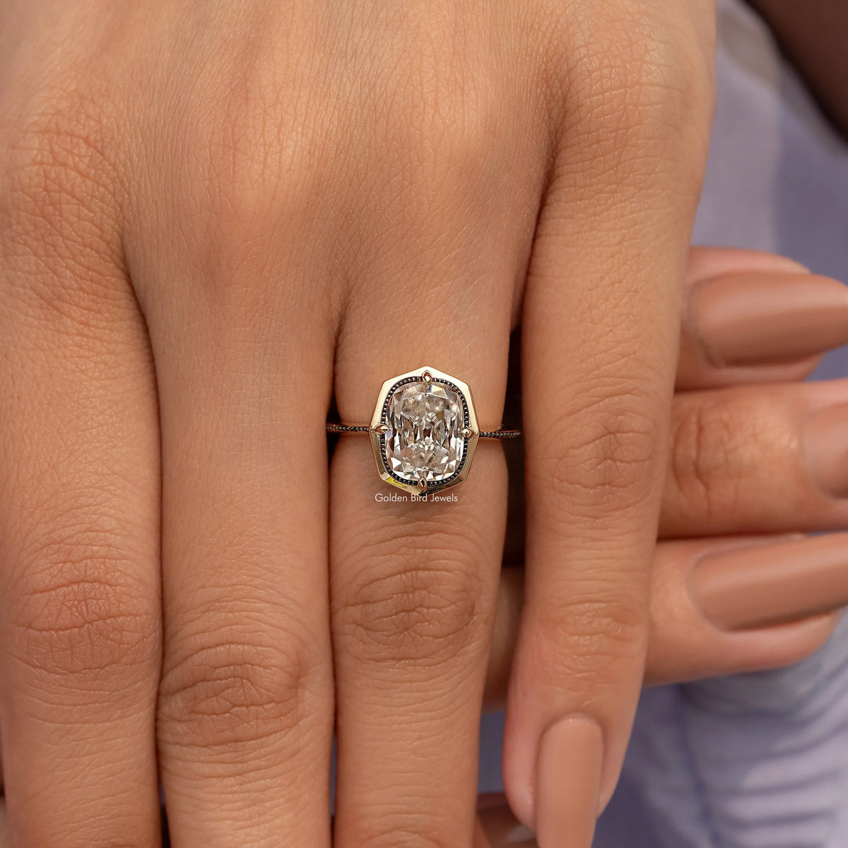 Gold-tone cushion-cut bezel set engagement ring with ornate band, close-up on hands