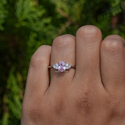 Oval pink gemstone engagement ring on palm with round side stones and slender band