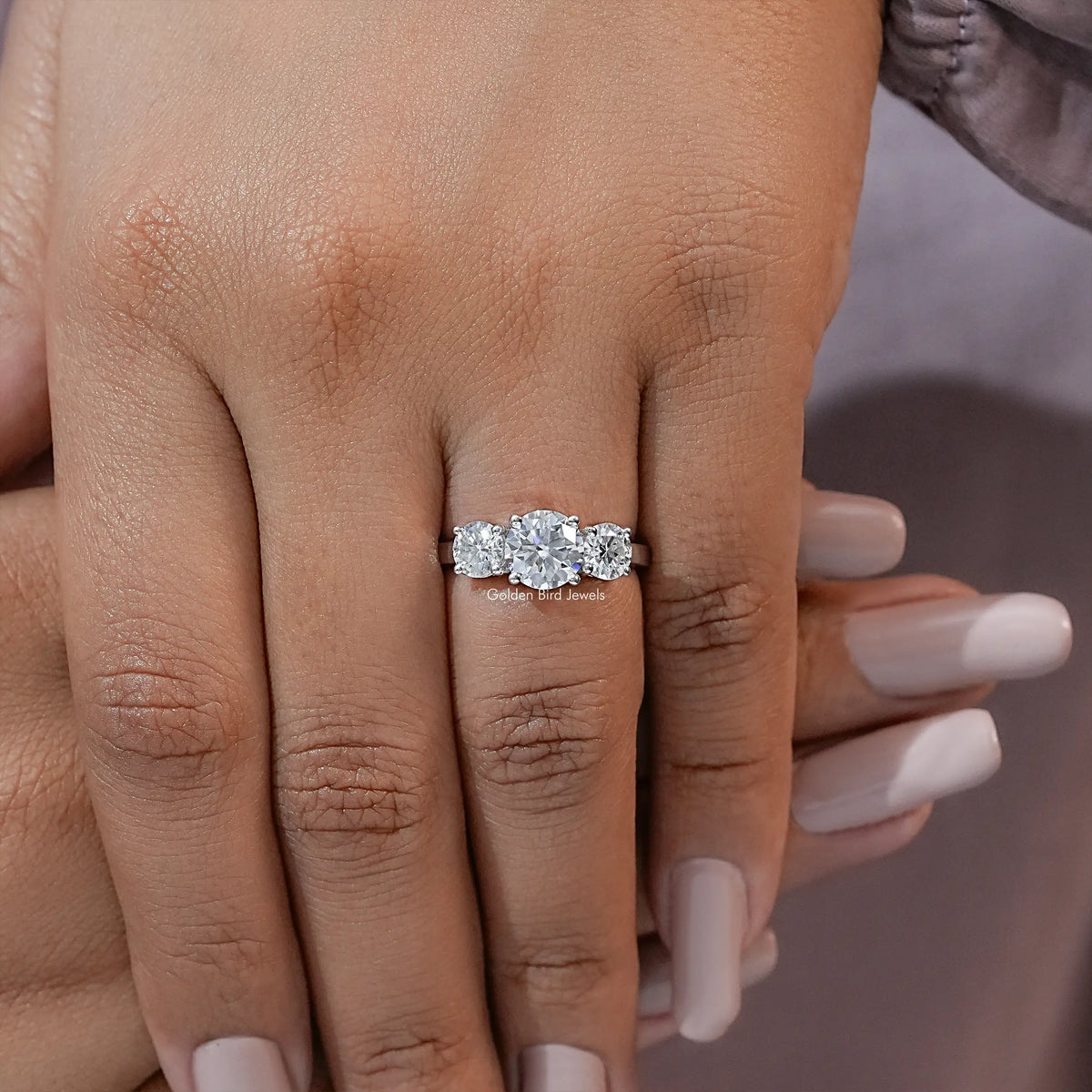 Three-stone moissanite ring on hand with round stones and slim silver shank