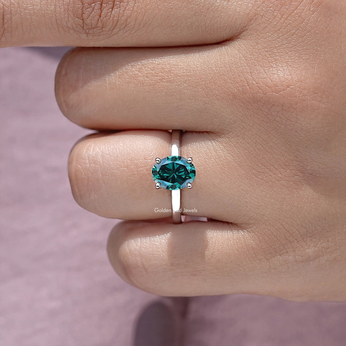 Oval teal moissanite center stone ring with hidden halo, close-up on hand