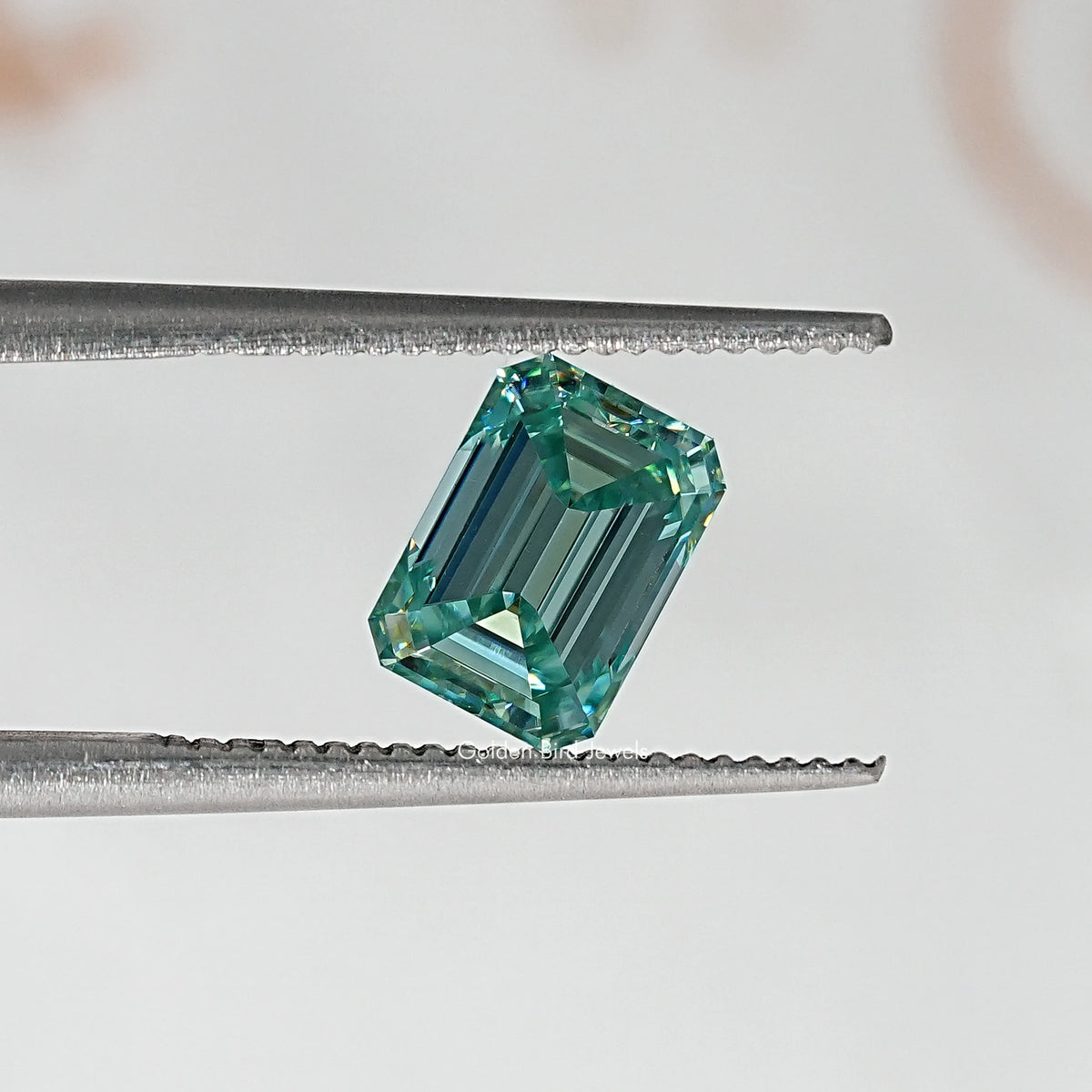 Emerald-cut green moissanite loose stone held between metal tweezers