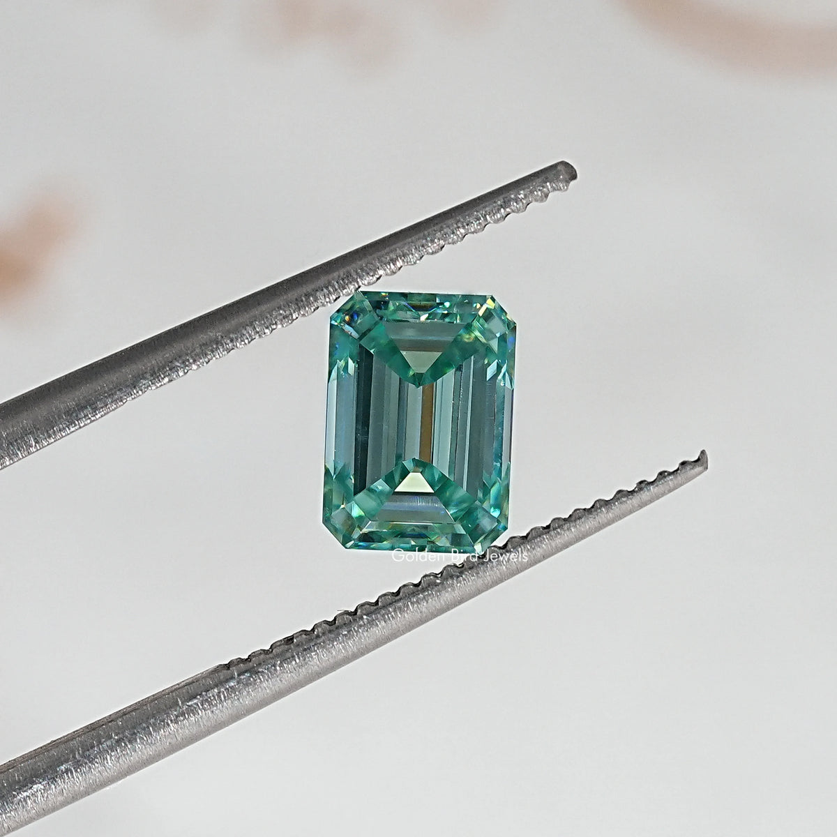 Emerald-cut green moissanite loose stone viewed with prongs from tweezers
