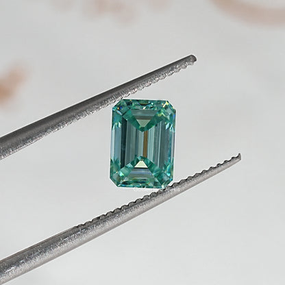 Emerald-cut green moissanite loose stone viewed with prongs from tweezers