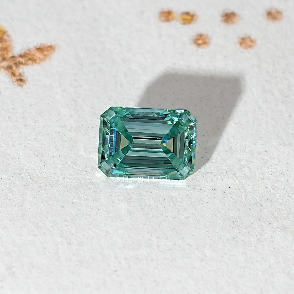 Emerald-cut teal-green moissanite loose stone centered on light surface