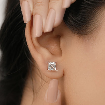 Asscher-cut moissanite stud earrings in white gold with square bezel stone.