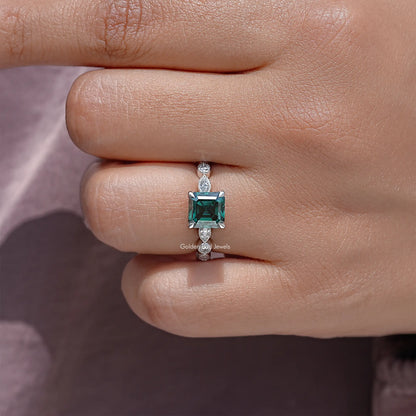 Green Asscher-cut moissanite ring on finger, silver prong setting and side sparkle stones