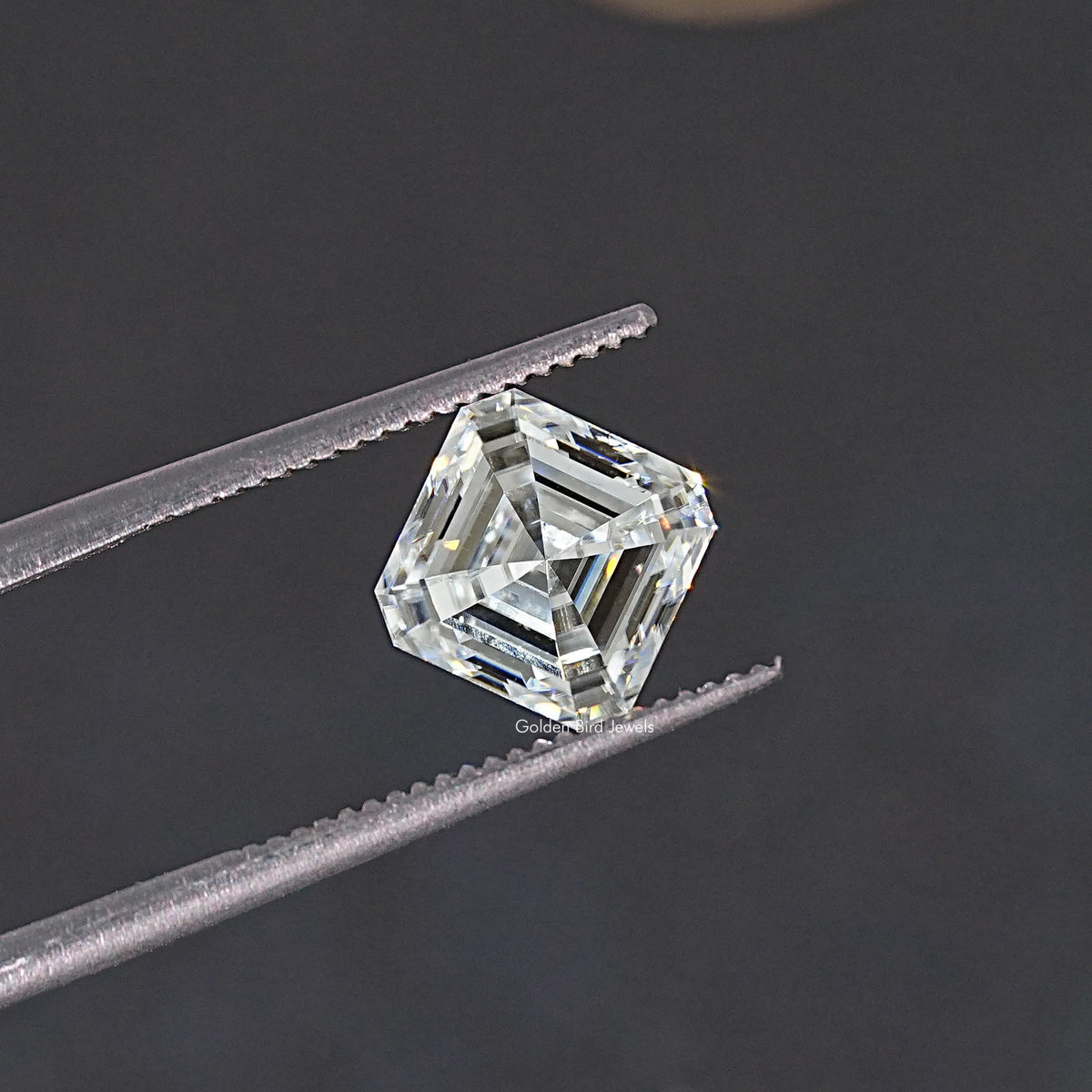 Asscher-cut colorless moissanite loose stone held between tweezers, profile angle