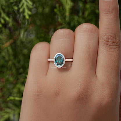 Oval teal moissanite bezel-set solitaire ring on finger, sterling silver band