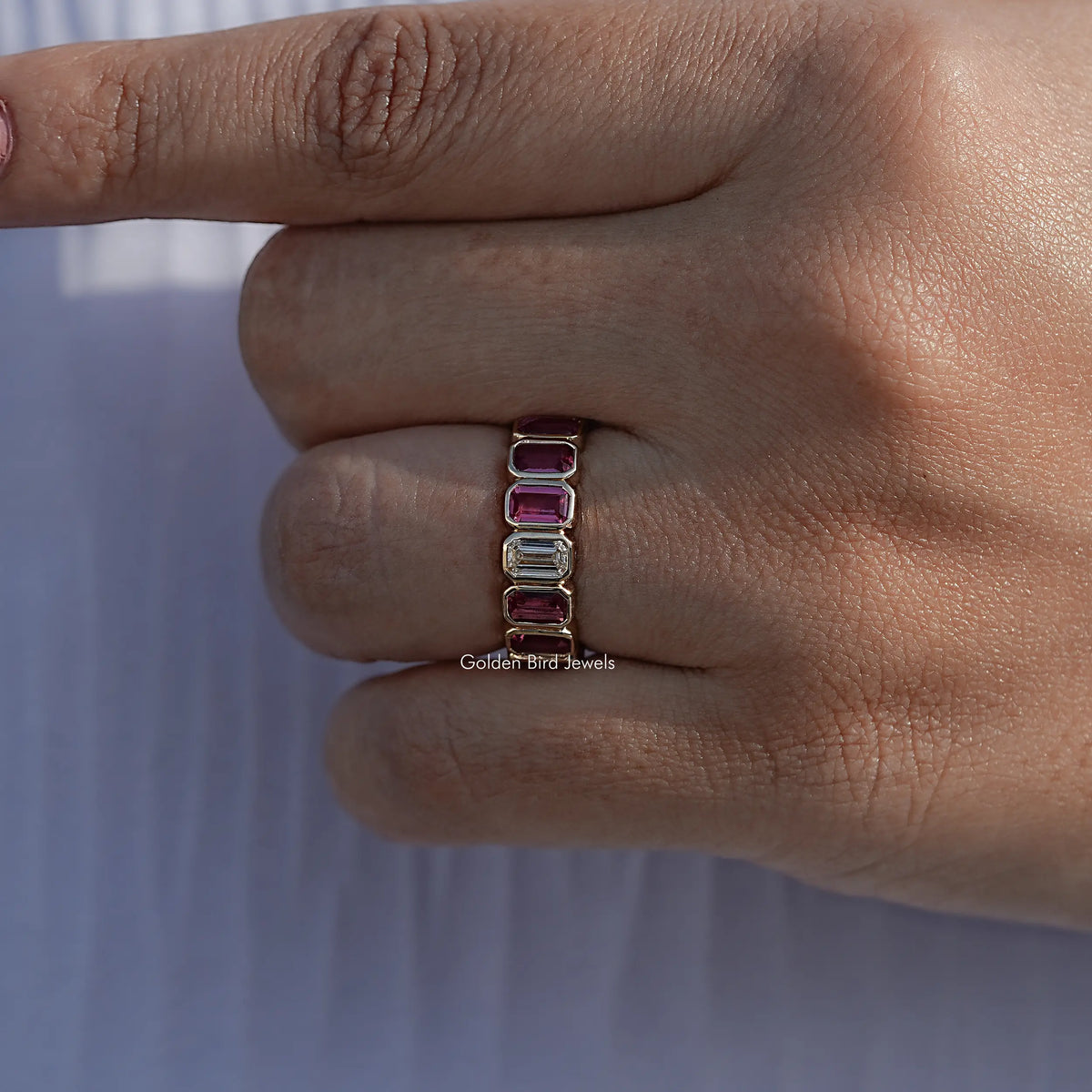Bezel-set eternity band with rectangular gemstones on finger, side view close-up