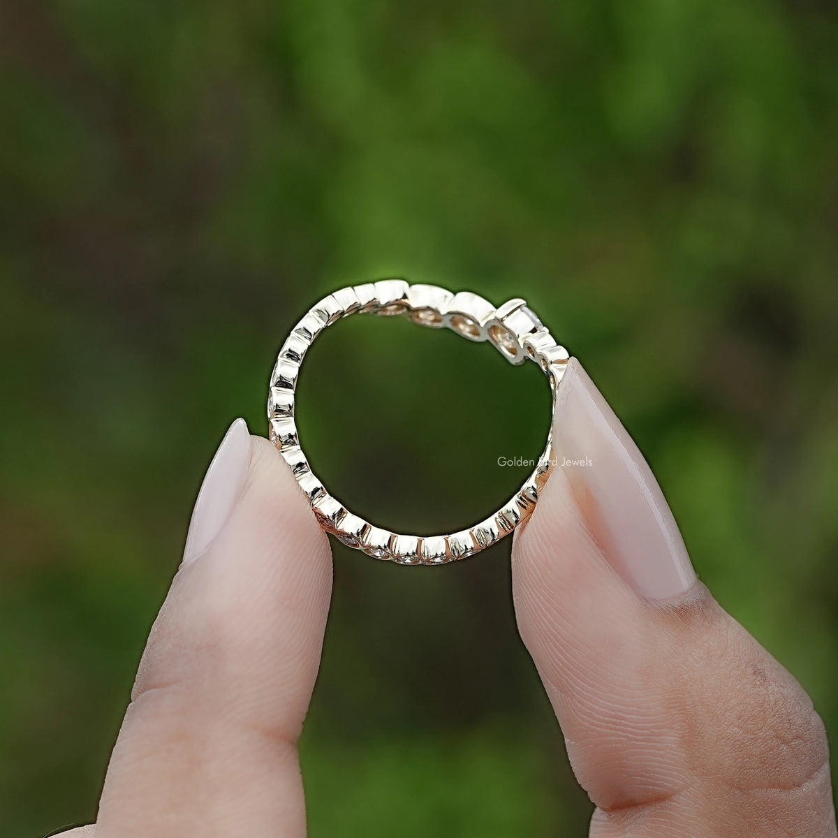 Silver curved eternity band ring with round stones, top view held between fingers