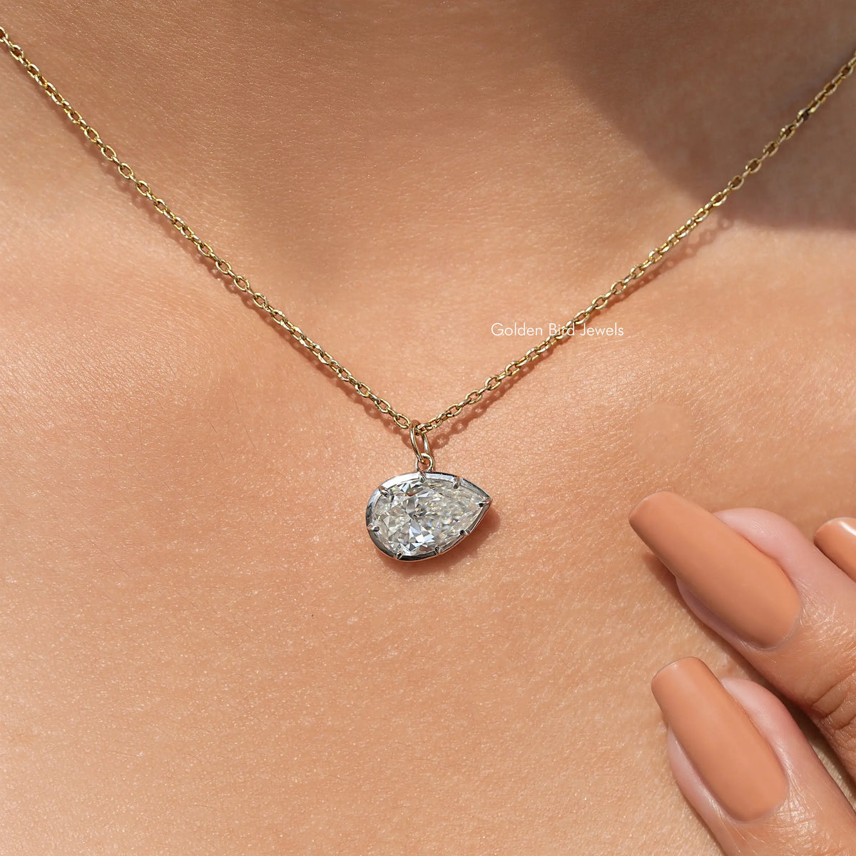 Gold-tone pear-shaped pendant on fine chain, shown near fingers