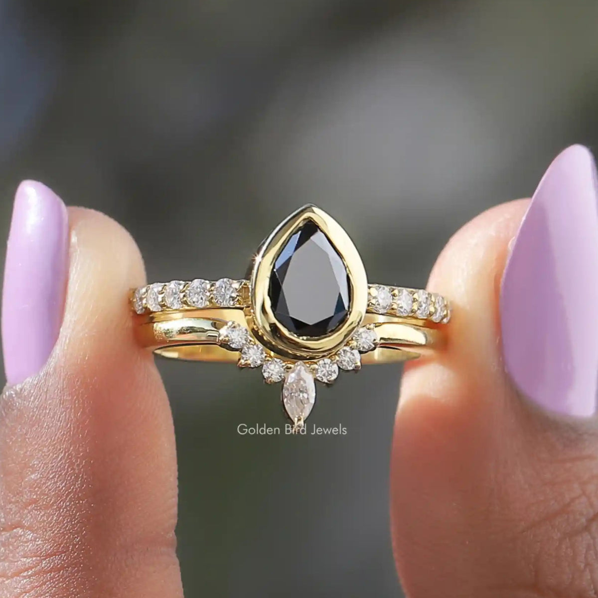 Two fingers holding the Black Pear Cut Moissanite Bridal Ring Set