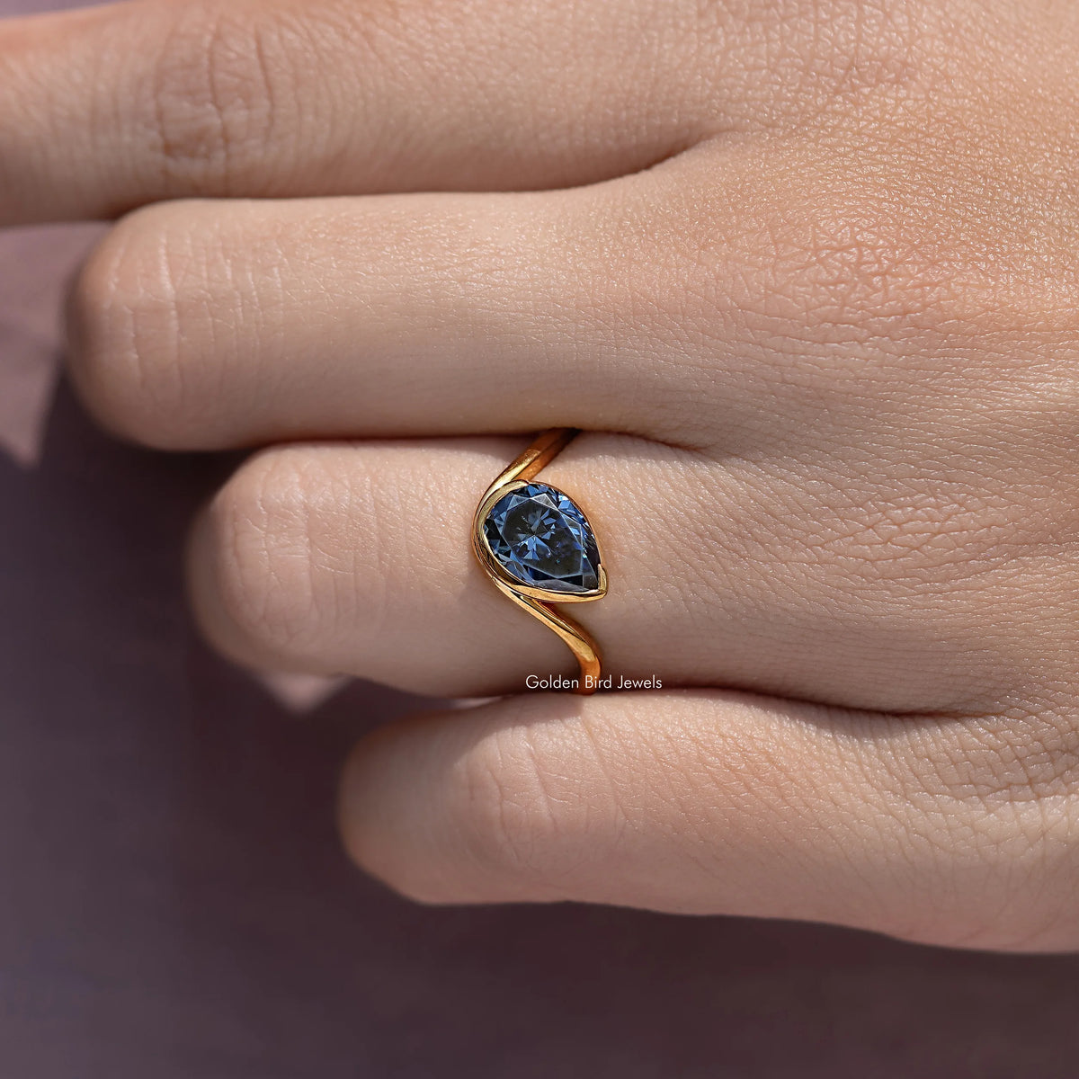 Close-up of curved solitaire ring with blue stone in gold twisted setting