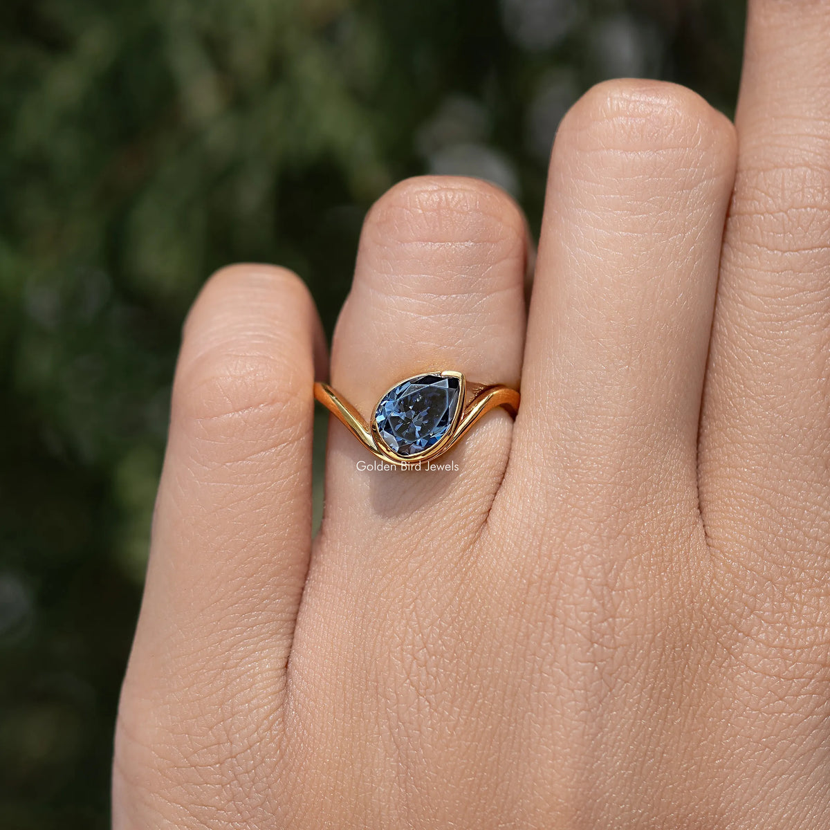 Curved ring with blue pear-cut center stone and flowing gold prongs