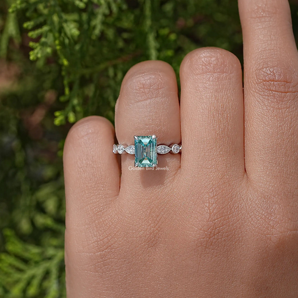 Silver emerald-cut moissanite ring, teal center stone with side round stones, front view.