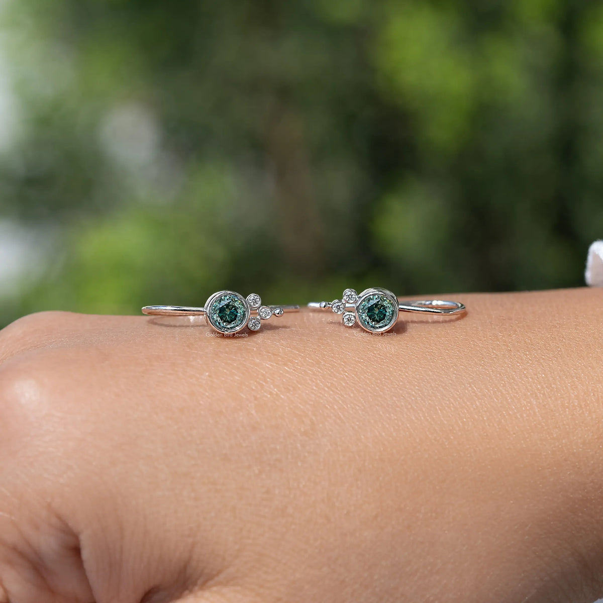 Silver round blue moissanite dangle earrings with halo, laid on wrist