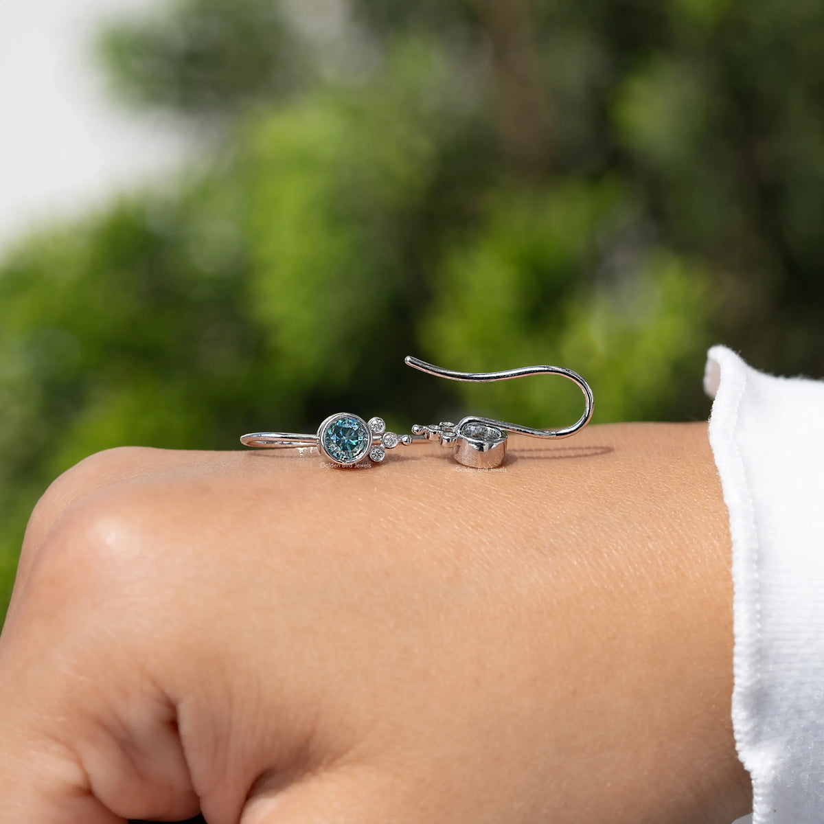 Silver round blue moissanite dangle earrings with open hook backs on wrist