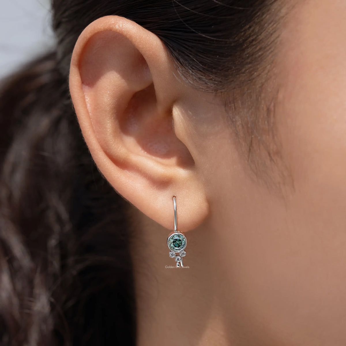 Silver round blue moissanite dangle earrings hanging from ear with blue center