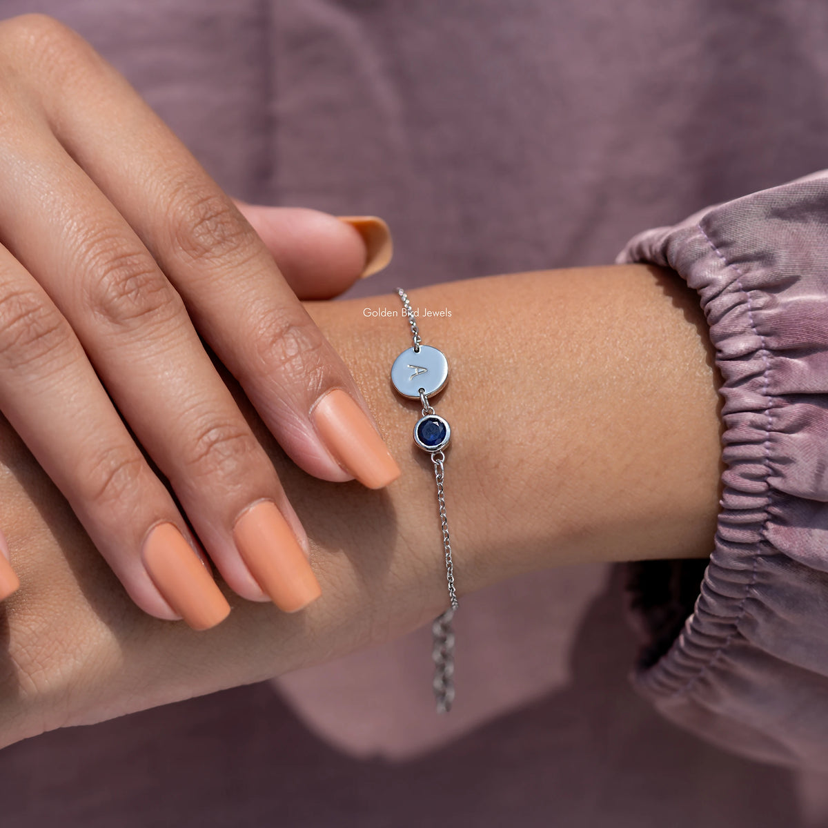 Bracelet on wrist: round light blue initial A charm with dark blue gemstone accent