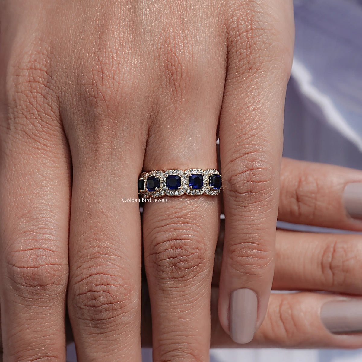 Blue five-stone gemstone halo band ring on hand, straight band with prong-set stones