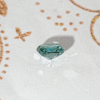 Elongated teal-green moissanite stone, side profile showing facet edges.