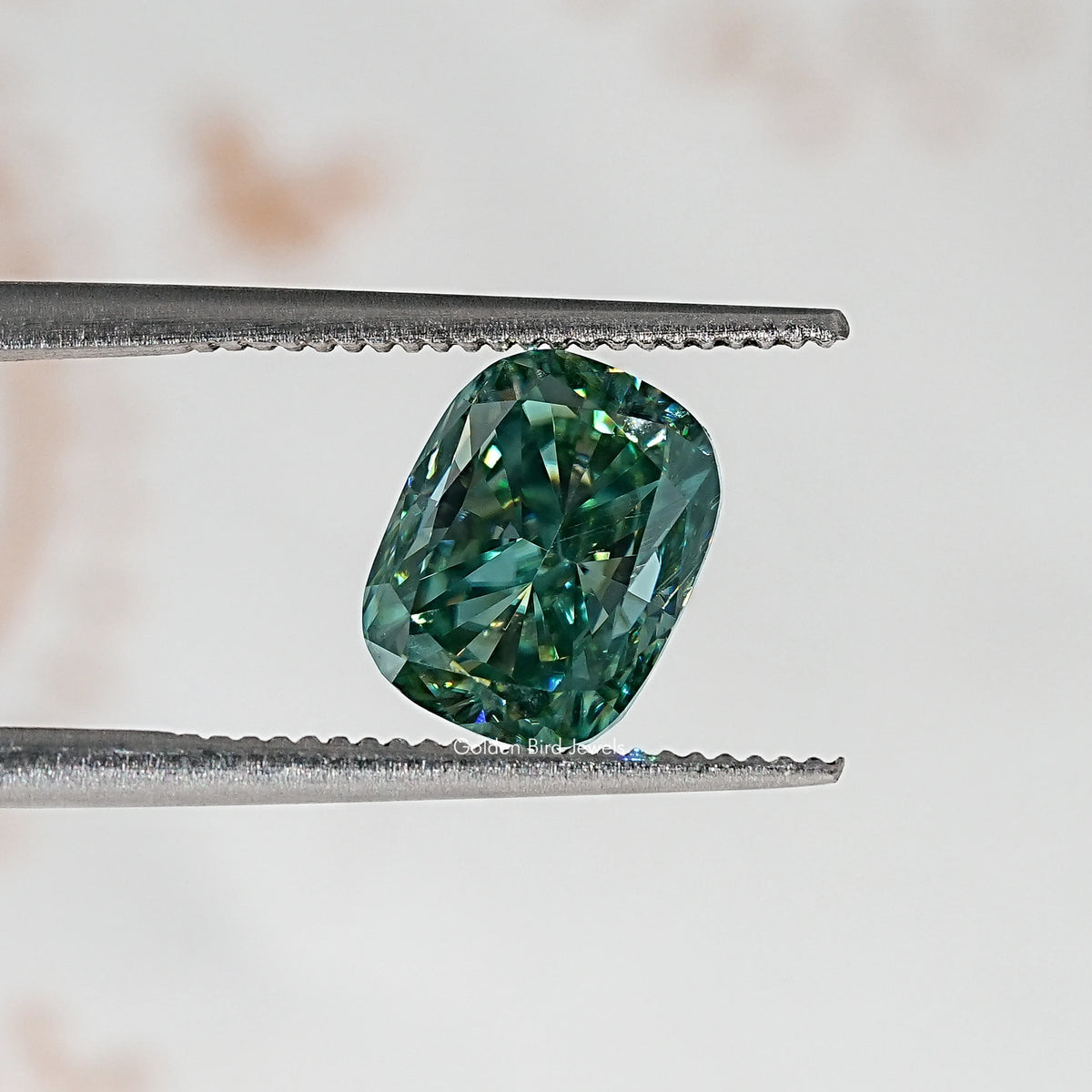 Elongated cushion teal-green moissanite stone, held by metal tweezers.