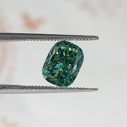Elongated cushion teal-green moissanite stone, held by metal tweezers.