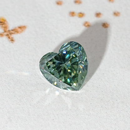 Loose heart-cut moissanite gemstone, deep green-blue with prismatic facets.