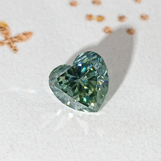 Loose heart-cut moissanite gemstone, deep green-blue with prismatic facets.
