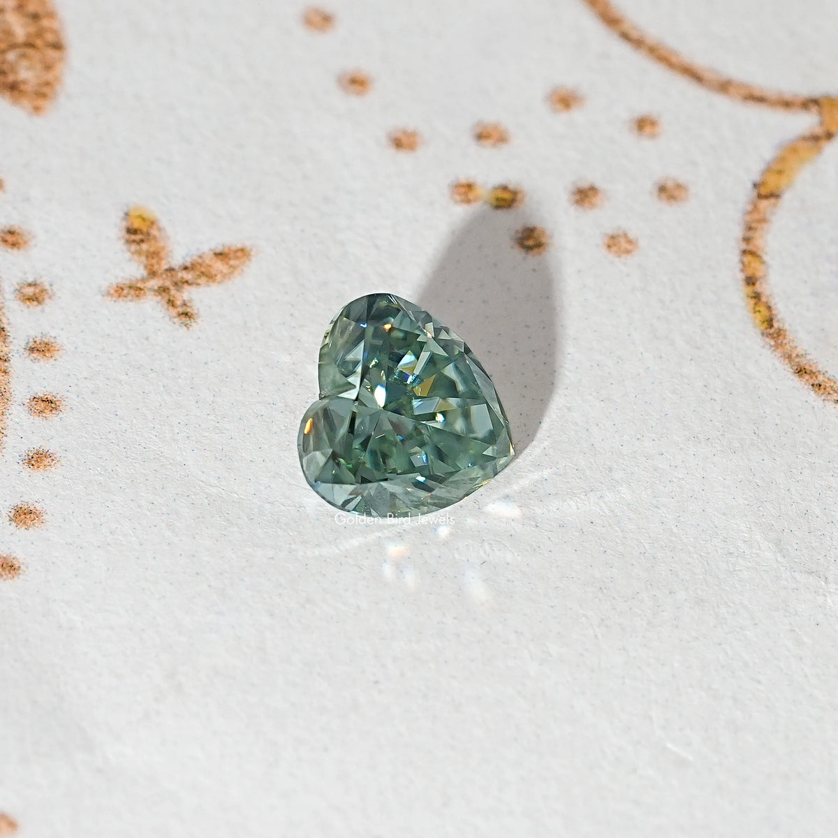 Loose heart-cut moissanite gemstone, green-blue color with faceted sparkle.