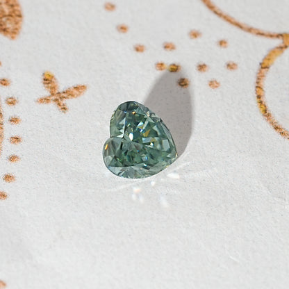 Loose heart-cut moissanite gemstone, green-blue color with faceted sparkle.