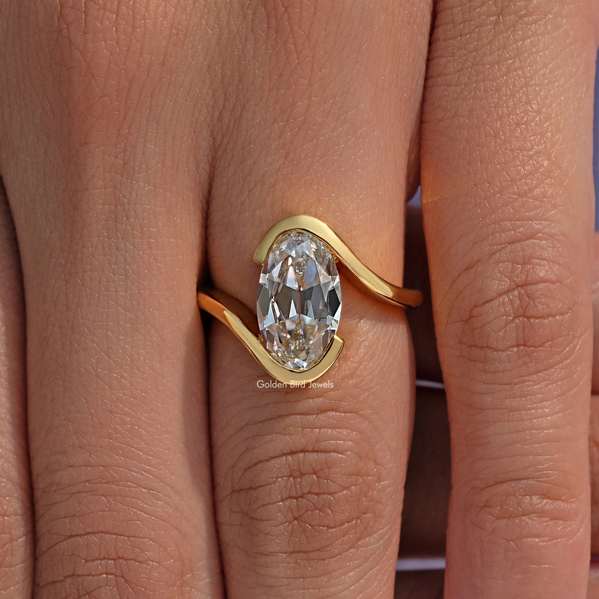 Gold-tone bypass solitaire ring with oval stone on finger, front view