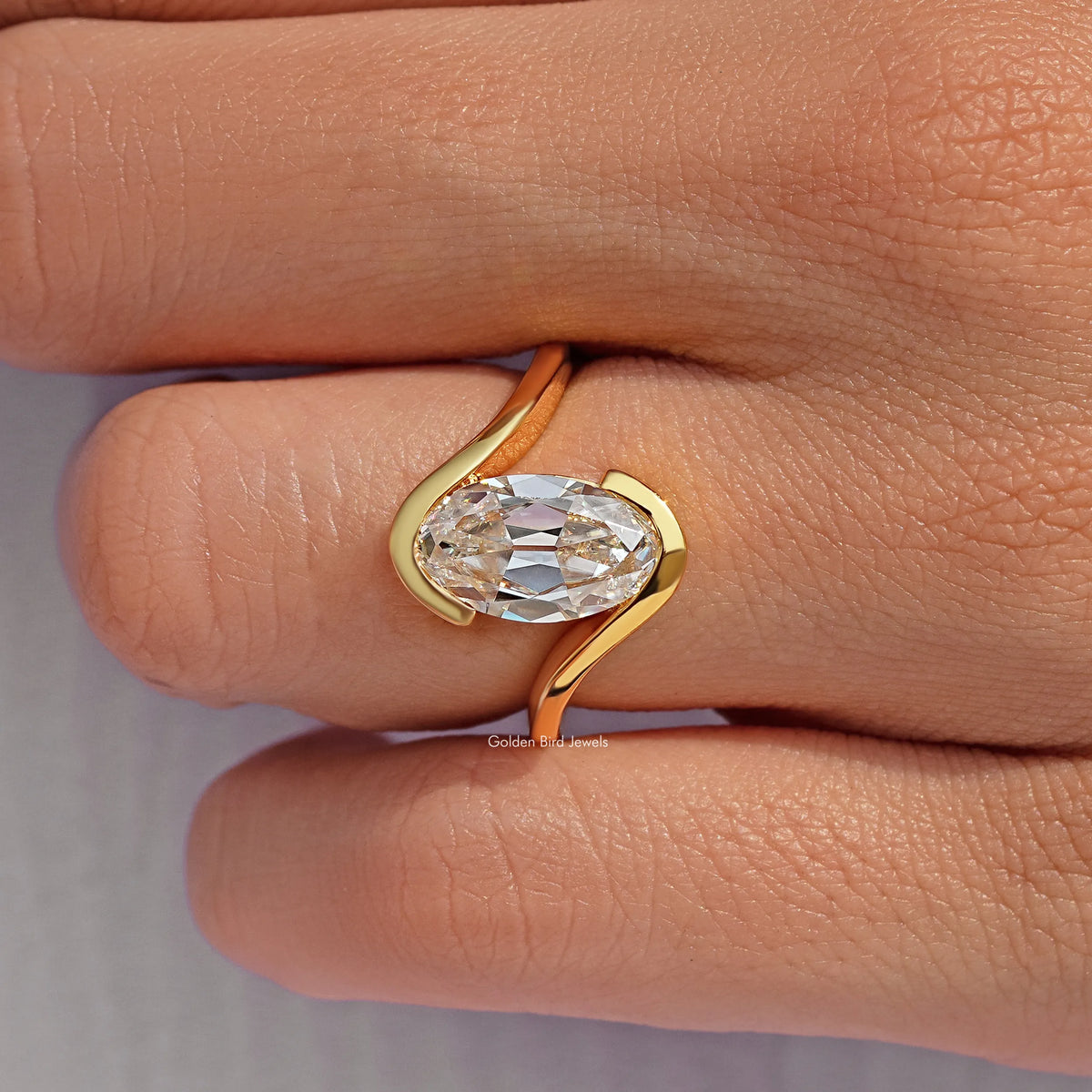 Gold-tone oval stone solitaire ring close-up, bypass band detail on finger